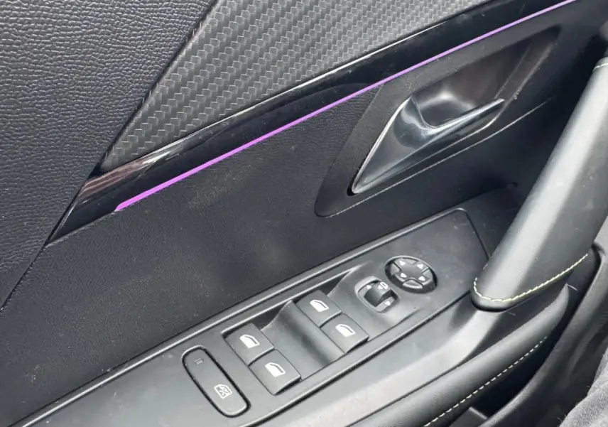 Gros plan sur la commande des vitres électriques côté conducteur d’une Peugeot 208 gris, avec insert décoratif noir et surpiqûres vertes.
