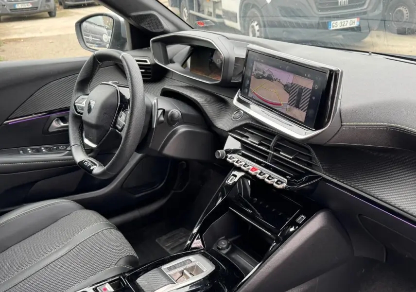 Vue intérieure côté conducteur de la Peugeot 208 Hybrid 110 e-DCS6 GT 2025, avec écran tactile et volant compact noir.
