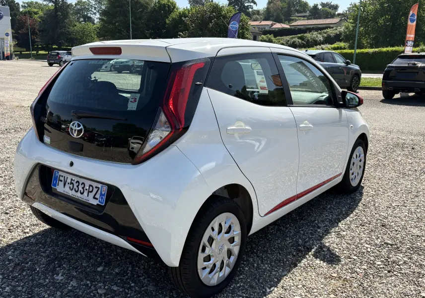 Vue 3/4 arrière droite d'une Toyota Aygo MC blanche 2020 avec toit noir et détails rouges sur le côté.