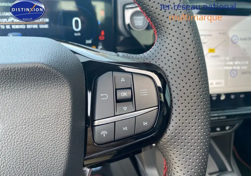 Gros plan sur les commandes au volant perforé avec surpiqûres rouges du Ford Puma rouge, tableau de bord et écran tactile en arrière-plan.