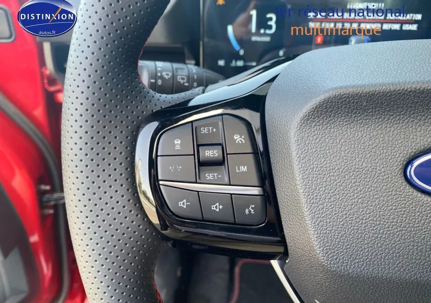 Gros plan sur les commandes au volant perforé avec surpiqûres rouges du Ford Puma rouge métallisé.