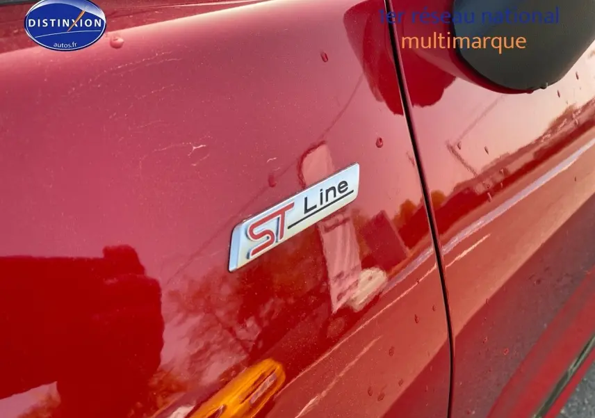 Gros plan sur l’écusson ST-Line côté gauche d’un Ford Puma rouge métallisé avec gouttes d’eau visibles.