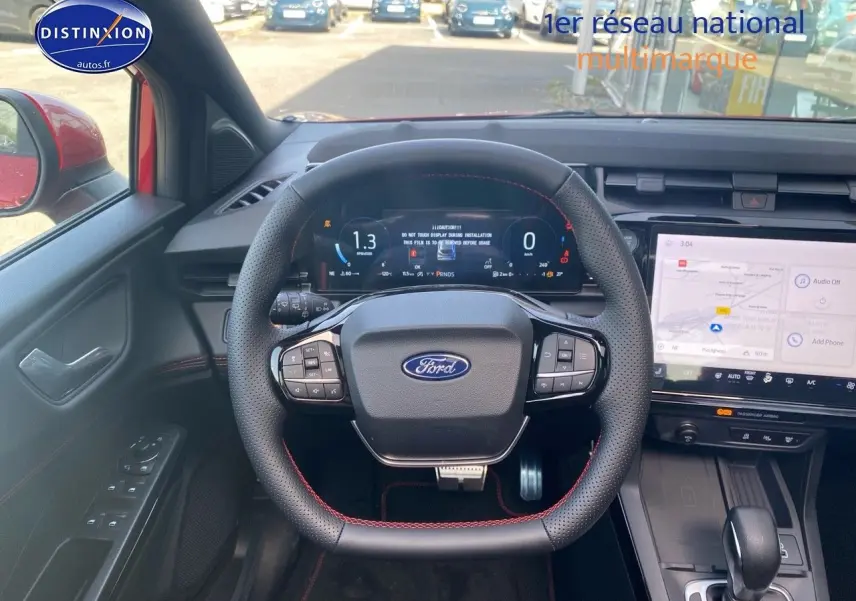 Vue intérieure centrée sur le volant noir avec surpiqûres rouges du Ford Puma rouge, écran tactile et tableau de bord numérique.