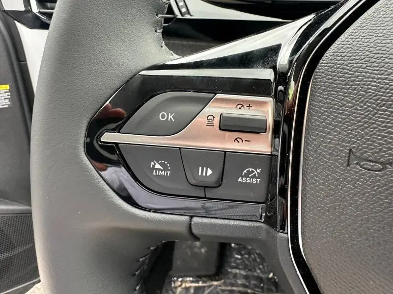 Gros plan sur les commandes de régulateur de vitesse au volant noir du Peugeot 308 blanc Okénite 2025.