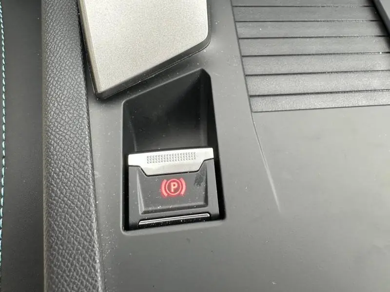 Gros plan sur le bouton de frein de stationnement électrique rouge dans la console centrale noire de la Peugeot 308 blanche.