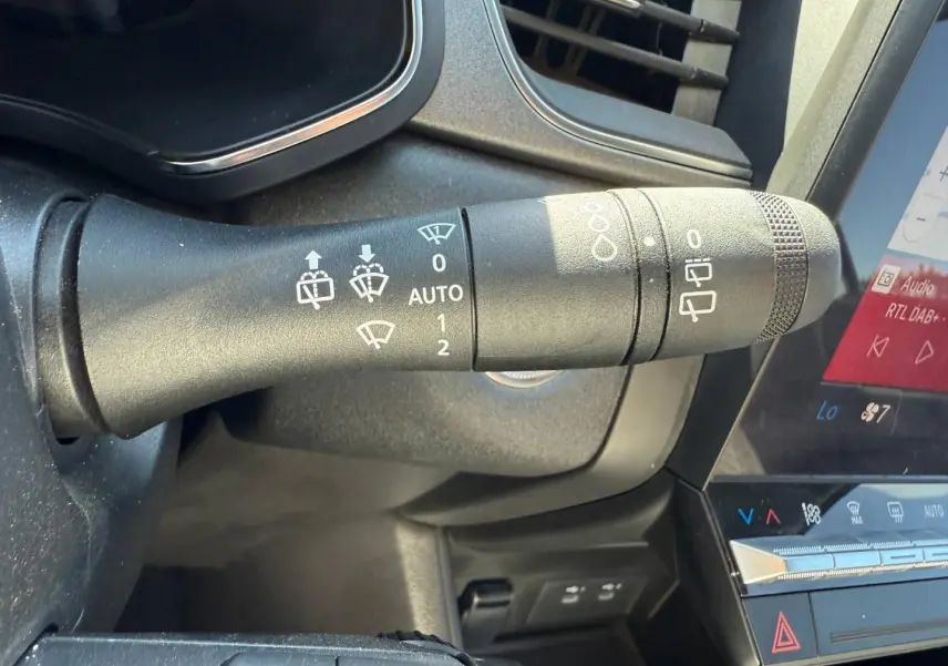 Gros plan sur la commande d’essuie-glace noire dans l’habitacle du Renault Captur gris métallisé, avec écran tactile visible.