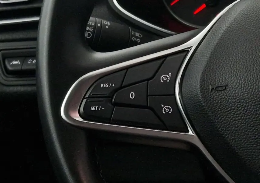 Gros plan sur les commandes de régulateur de vitesse au volant d'une Renault Clio V gris platine, intérieur sombre.