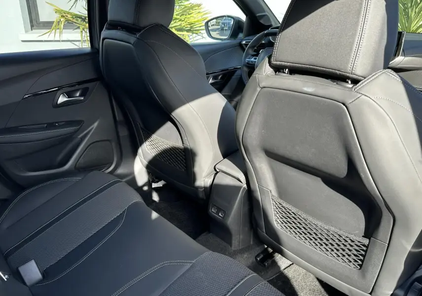 Vue arrière intérieure montrant les sièges noirs et les ports USB à l'arrière des sièges avant du Peugeot 208 Hybrid 145 GT.