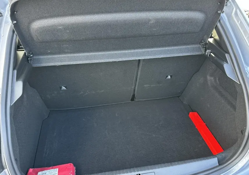 Coffre ouvert d'une Peugeot 208 Hybrid 145 gris Artense, montrant un espace de rangement vide avec un triangle de signalisation rouge.