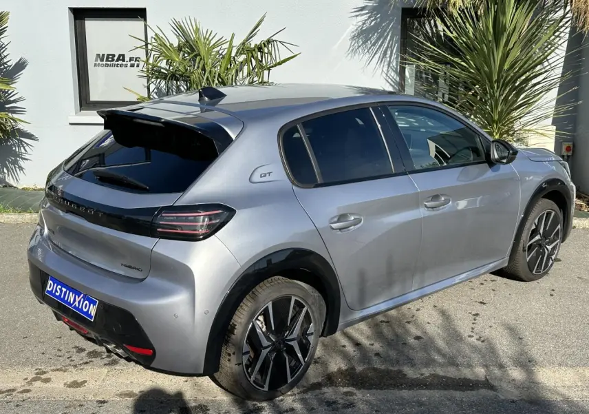 Vue 3/4 arrière droite d'une Peugeot 208 Hybrid 145 GT gris Artense avec jantes alliage bi-tons et badge GT sur l'aile arrière