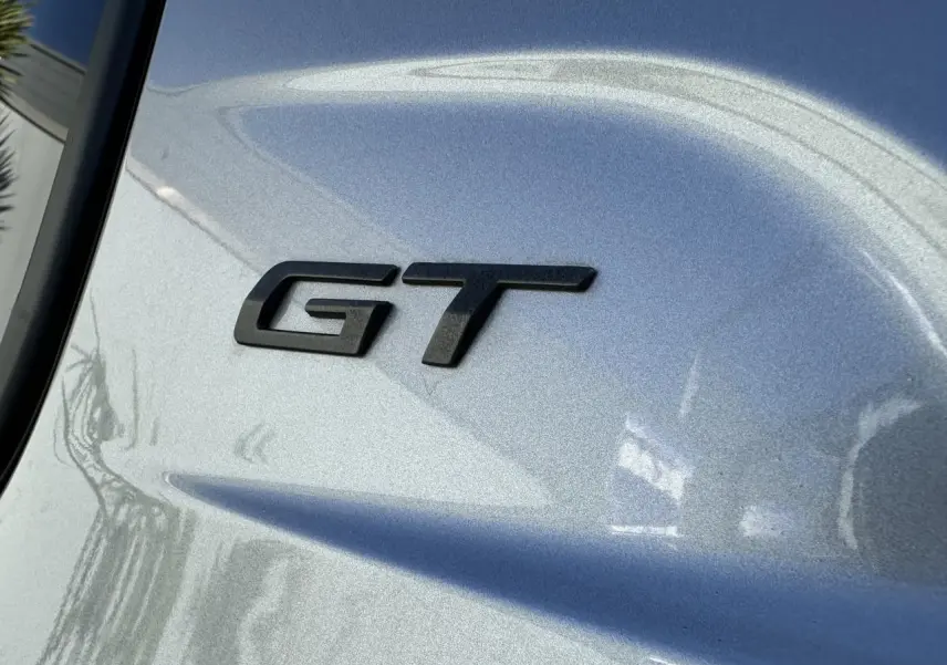 Gros plan sur l’inscription GT noire sur la carrosserie gris Artense d’une Peugeot 208 Hybrid 145 e-DSC6 GT.