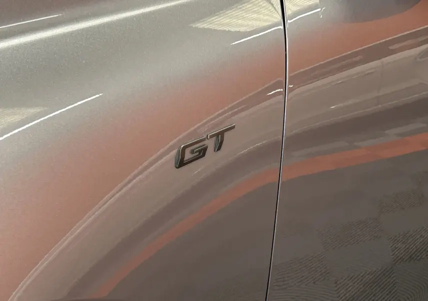 Gros plan sur l'emblème GT noir sur la porte avant côté gauche d'une Peugeot 508 SW gris artense brillante.