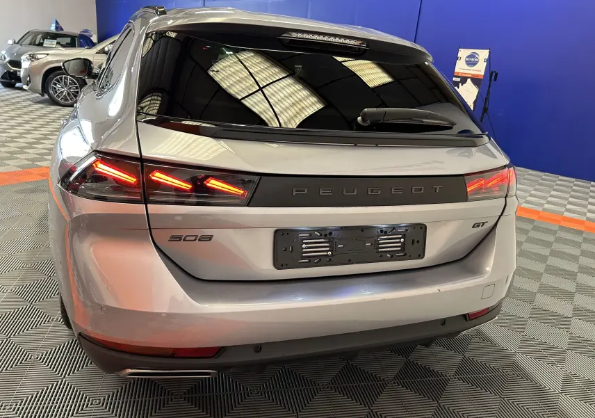 Vue arrière en léger 3/4 droit d'une Peugeot 508 SW GT gris artense avec feux LED allumés dans un showroom.