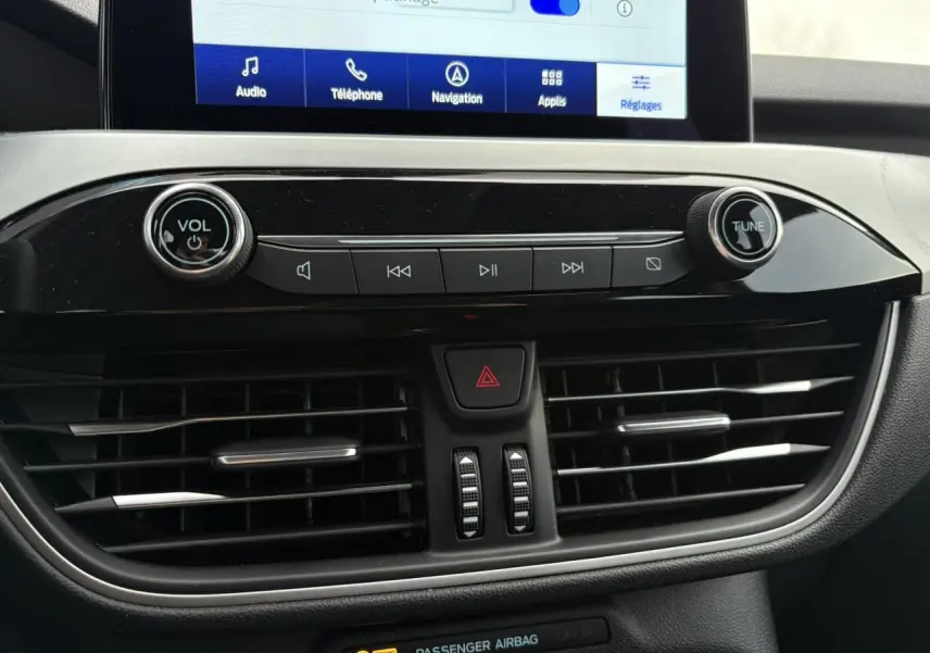 Vue rapprochée de la console centrale du Ford Kuga 2024, avec écran tactile et commandes audio noires brillantes.