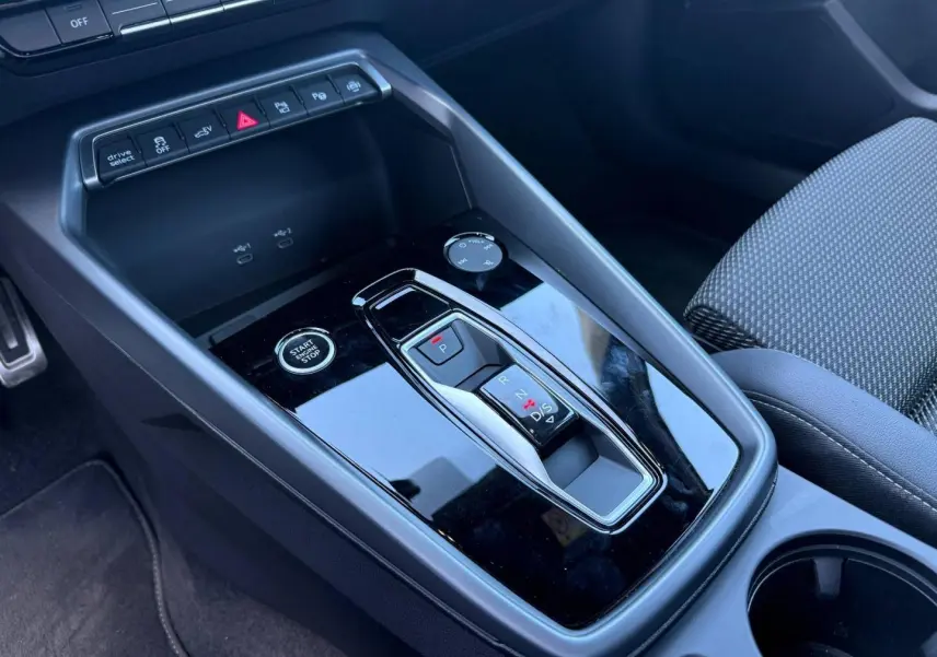 Gros plan sur la console centrale noire brillante de l’Audi A3 Sportback 2025 avec levier de vitesse automatique et bouton start/stop.