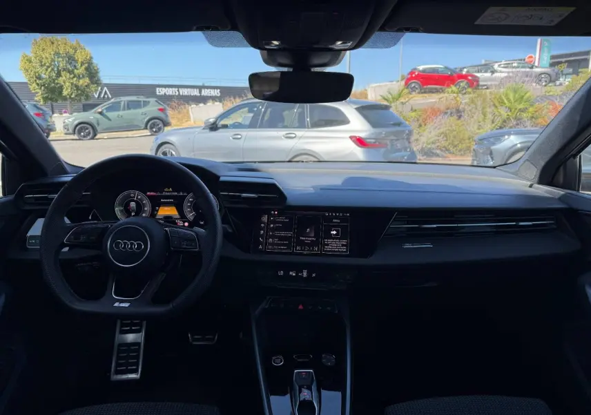 Vue intérieure avant de l'Audi A3 Sportback 2025 hybride, tableau de bord noir avec volant sport et écran tactile central.