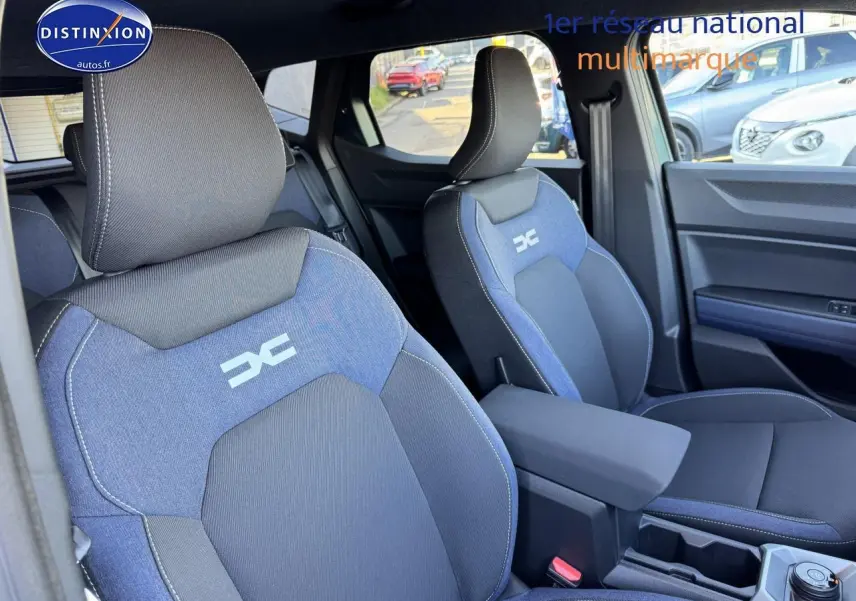 Vue intérieure rapprochée des sièges avant bleu et noir du Dacia Duster 2025 avec accoudoir central et logo distinctif brodé.