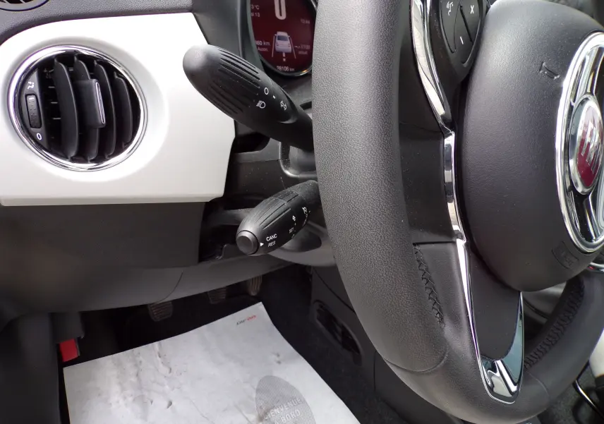 Gros plan sur le volant noir et la console blanche de la FIAT 500 2019, avec commandes au volant visibles.