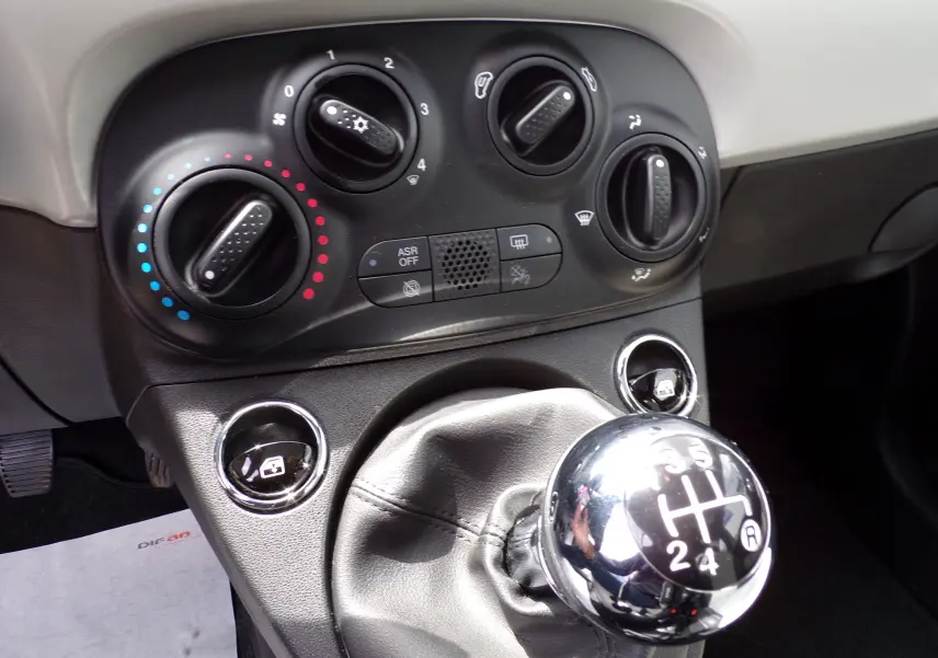 Gros plan sur la console centrale de la Fiat 500 blanche 2019, mettant en valeur la commande de climatisation et le levier de vitesses manuel chromé.