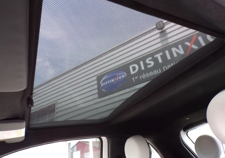 Toit panoramique en verre avec pare-soleil sur l'intérieur d'une Fiat 500 blanche, vue de l'habitacle vers le haut.