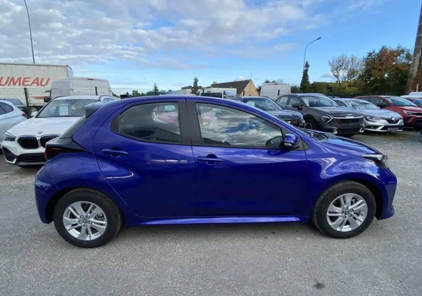 Profil côté gauche d'une Toyota Yaris 2025 hybride bleu Genièvre avec jantes alliage 15 pouces sur parking.