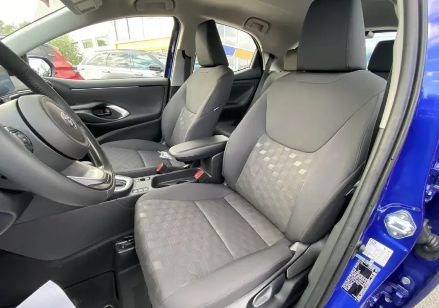 Vue intérieure côté conducteur de la Toyota Yaris 2025 bleu Genièvre, montrant les sièges avant en tissu gris et la porte ouverte.