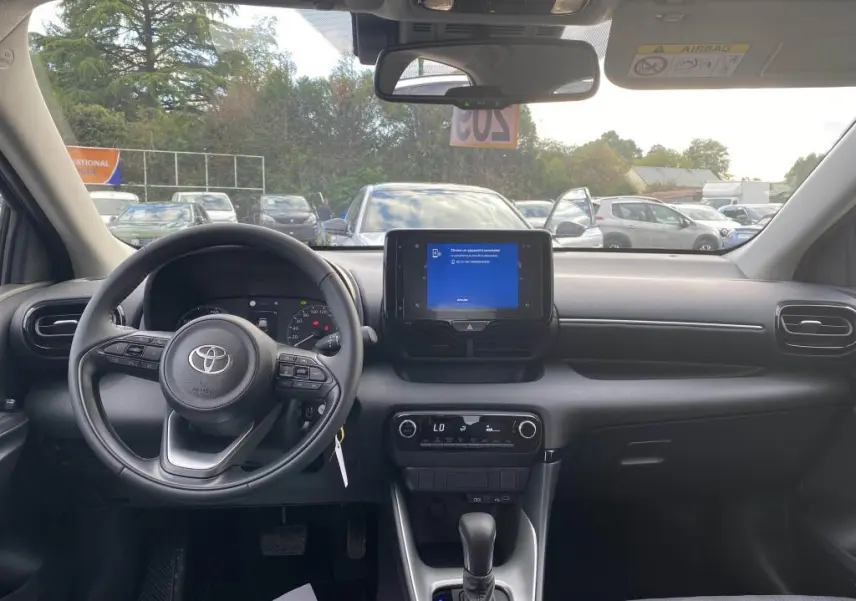 Vue intérieure frontale du tableau de bord et volant de la Toyota Yaris hybride 2025, avec écran tactile central allumé.