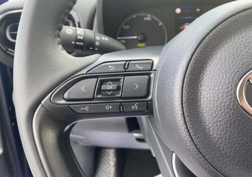 Gros plan sur les commandes au volant côté gauche de la Toyota Yaris hybride 2025, intérieur noir.