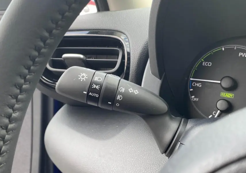 Gros plan sur la commande d'éclairage à gauche du volant dans l'habitacle d'une Toyota Yaris hybride 2025 Bleu Genièvre.
