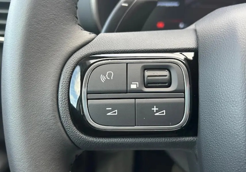 Gros plan sur les commandes noires du volant en cuir du Citroën C5 Aircross 2025, version diesel bleu Eclipse Metal.