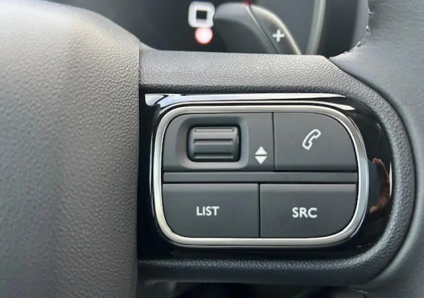 Gros plan sur les commandes gauche du volant noir du Citroën C5 Aircross 2025, boutons pour appels et listes.