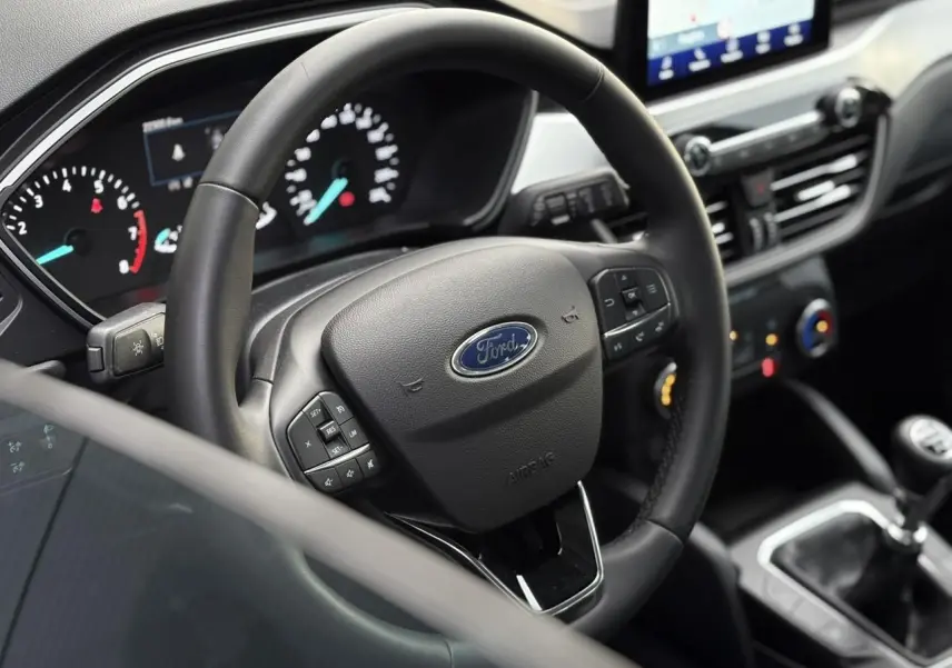 Vue intérieure rapprochée du volant en cuir multifonctions du Ford Kuga 2024 avec tableau de bord et console centrale visibles.