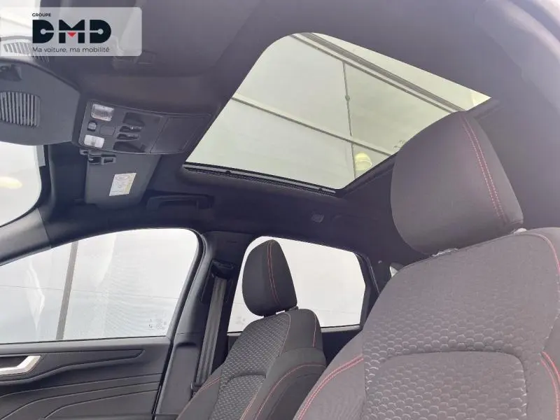 Vue intérieure du Ford Kuga 2026 montrant les sièges avant noirs avec surpiqûres rouges et toit ouvrant panoramique.
