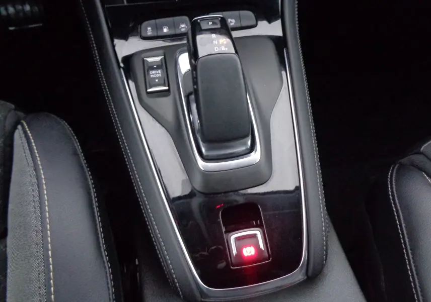 Gros plan sur la console centrale noire brillante de l'Opel Grandland X hybride, avec levier de vitesses automatique et frein à main électronique.