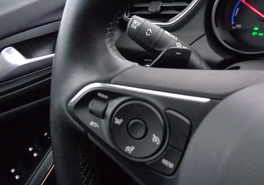 Gros plan sur les commandes au volant noir de l'Opel Grandland X hybride rechargeable, avec tableau de bord partiellement visible.