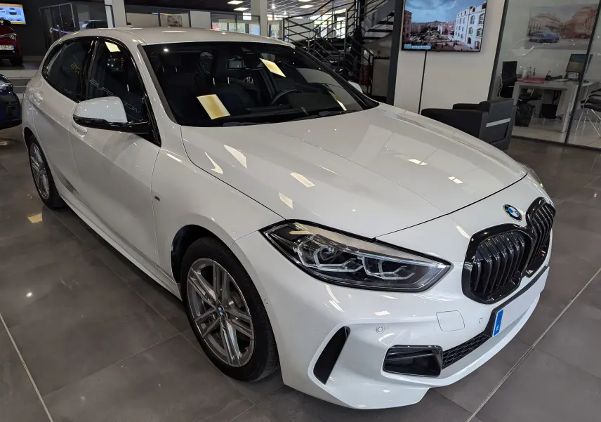 BMW Série 1 F40 blanc alpin vue 3/4 avant droit en showroom, avec calandre noire et jantes alliage grises.