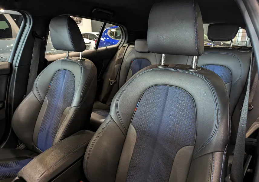Vue intérieure sur les sièges avant en cuir noir et tissu bleu avec surpiqûres bleues de la BMW Série 1 F40 M Sport.