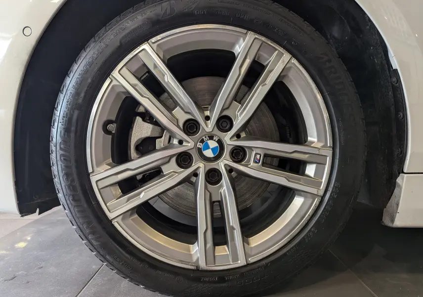 Gros plan sur la jante alliage M sport argentée d'une BMW Série 1 F40 blanc alpin, avec logo BMW central visible.