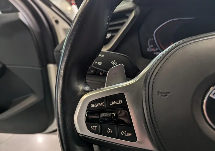 Gros plan sur les commandes de régulateur de vitesse au volant cuir noir d'une BMW Série 1 F40 blanche.