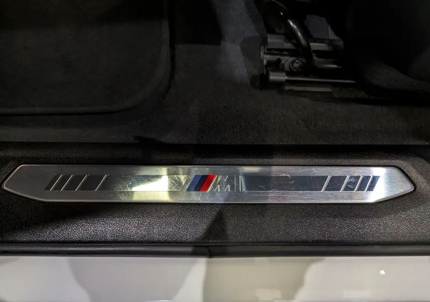 Gros plan sur la plaque de seuil M Sport en métal brossé dans l'entrée côté gauche d'une BMW Série 1 Blanc Alpin.