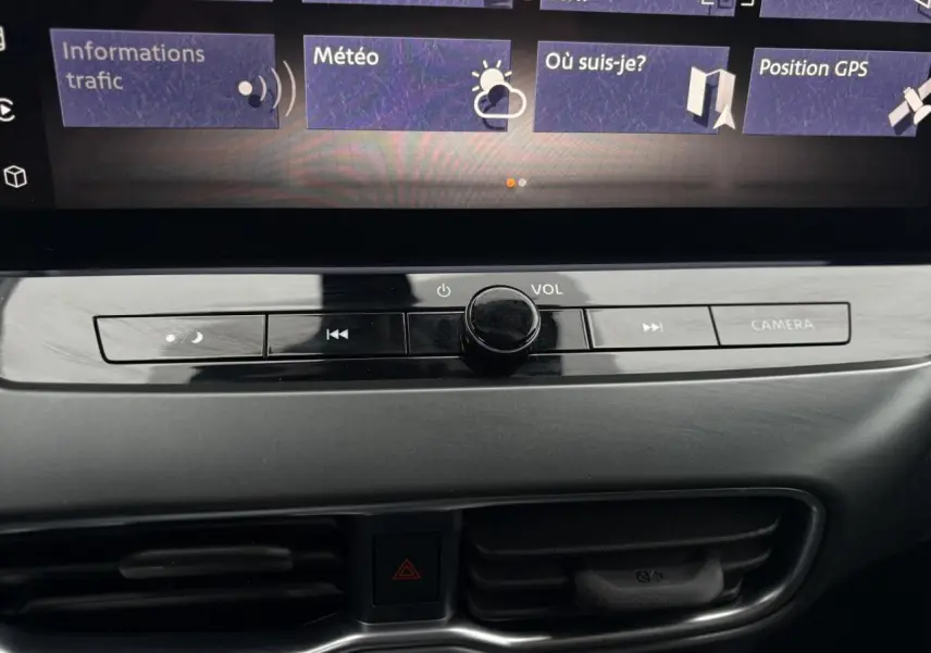 Gros plan sur la console centrale du Nissan Juke blanc nacré 2025, avec commandes volume et bouton caméra visibles.