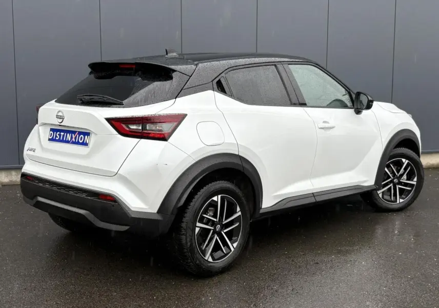 Nissan Juke blanc nacré vue 3/4 arrière droit sous la pluie avec toit noir et jantes alliage 17 pouces.