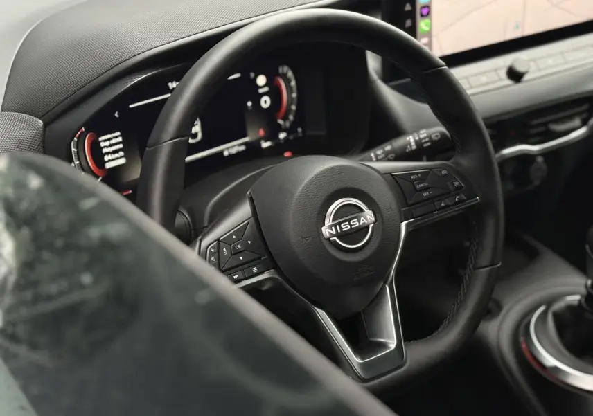 Vue rapprochée du volant en cuir noir du Nissan Juke 2025 avec tableau de bord digital et console centrale.