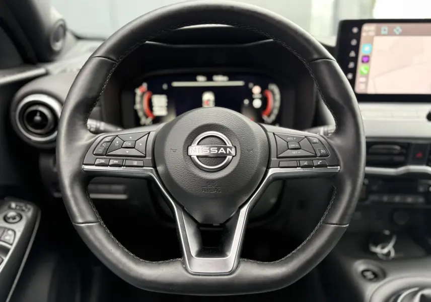 Volant en cuir noir de Nissan Juke 2025 avec commandes intégrées, tableau de bord digital et écran tactile visible en arrière-plan.