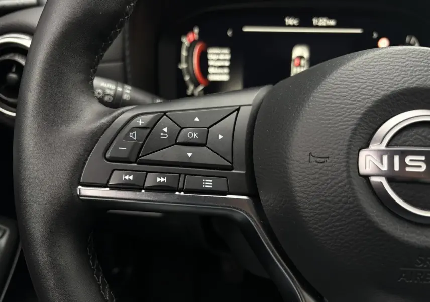 Gros plan sur le volant en cuir noir côté gauche du Nissan Juke 2025 avec commandes multifonctions et tableau de bord digital flou.