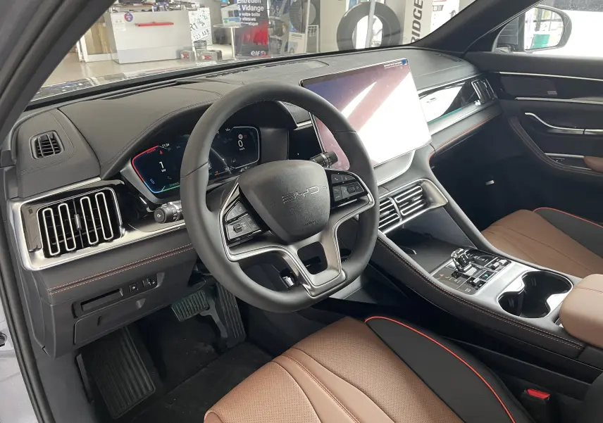 Vue intérieure côté conducteur du BYD SEAL U 2025 avec sellerie marron et noire, volant multifonction et écran tactile central.