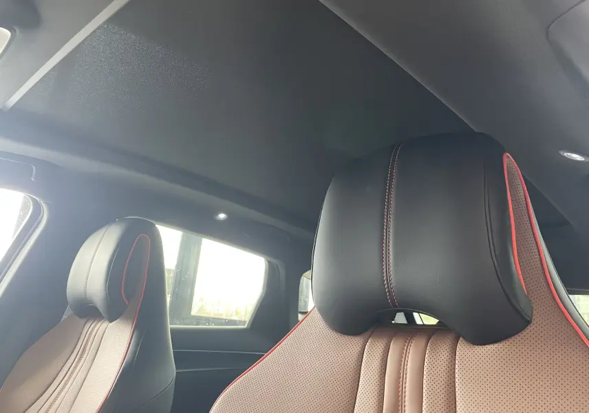 Gros plan sur les sièges avant en similicuir vegan noir et marron avec surpiqûres rouges dans l'habitacle sombre.