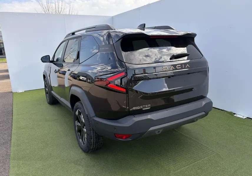 Vue 3/4 arrière droite du Dacia Bigster noir nacré avec signature lumineuse LED et barres de toit noires.