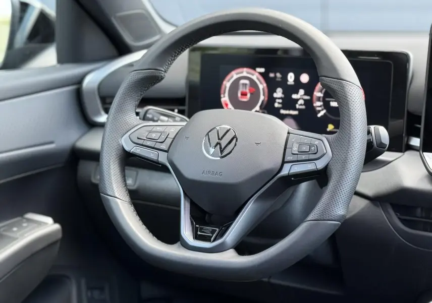 Vue rapprochée du volant sport multifonction noir du Volkswagen T-Roc 2026 avec tableau de bord numérique en arrière-plan.
