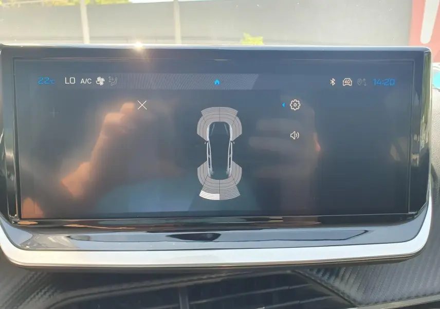 Écran tactile central de la Peugeot 208 1.2 Hybrid 110, affichant l'aide au stationnement avec vue de dessus du véhicule.